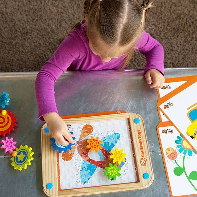 A focused young child assembles a vibrant gear-themed puzzle on a table, carefully connecting colorful gears to complete the design.