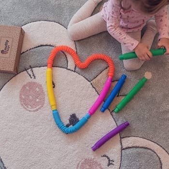 A heart shape created from colorful pop tube sensory toys with a child model holding a green tube.