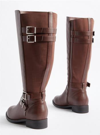 Two brown knee-high boots featuring decorative buckles at the top and ankle, paired with a low heel. Displayed on a white background.