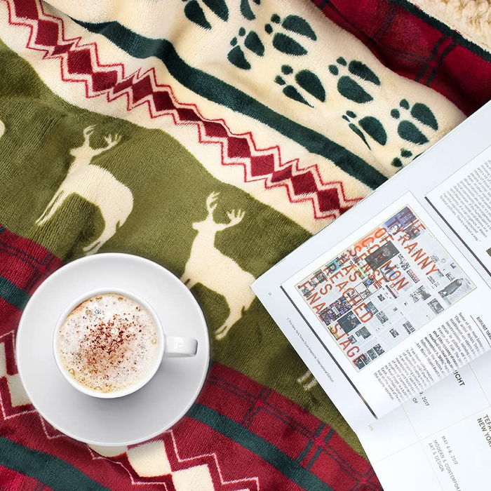 A close-up shot showcasing a mug and a magazine placed on top of the reindeer-print throw blanket, highlighting its pattern