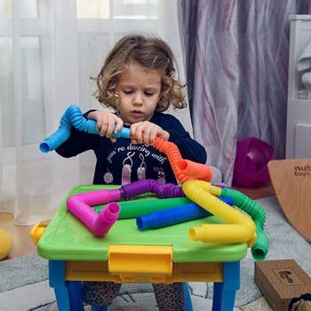 A child model joining together blue and orange pop sensory tubes.