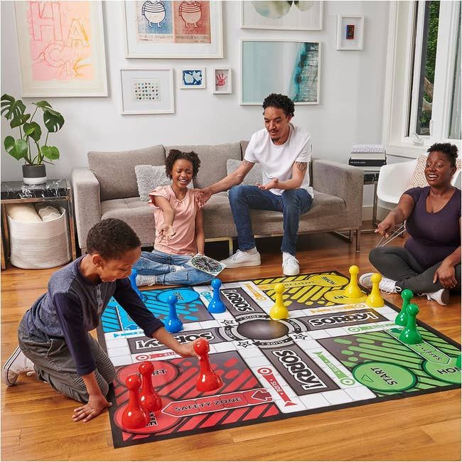 A family of four engaging in a large-scale version of the Sorry! board game on the floor.