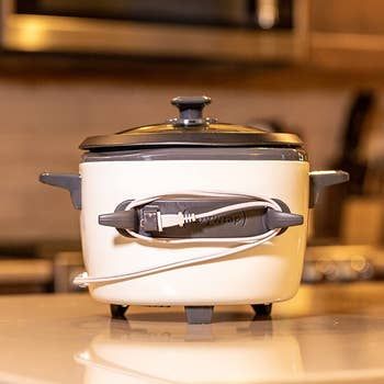 A gray, oval-shaped rubber adhesive with two prongs attached to a slow cooker, with the cord neatly wrapped around it.