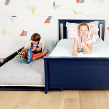 two kids lounging on a navy trundle bed