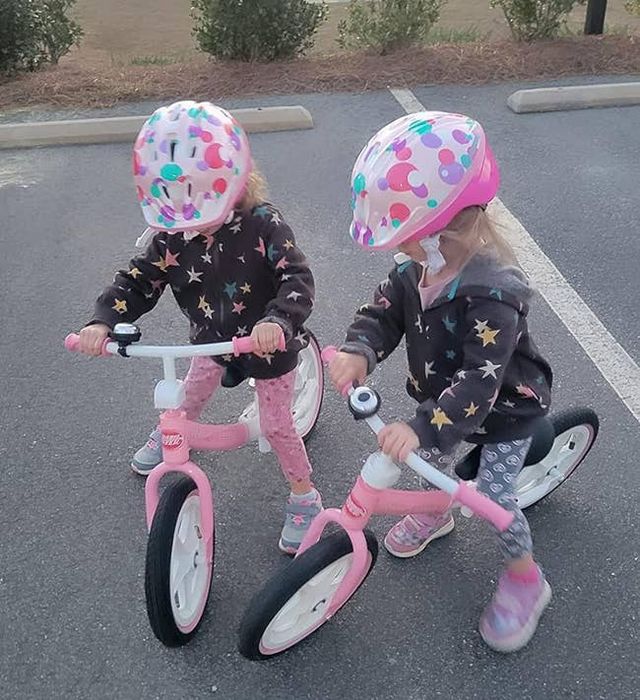 Two kids sporting polka-dot helmets, riding their balance bikes