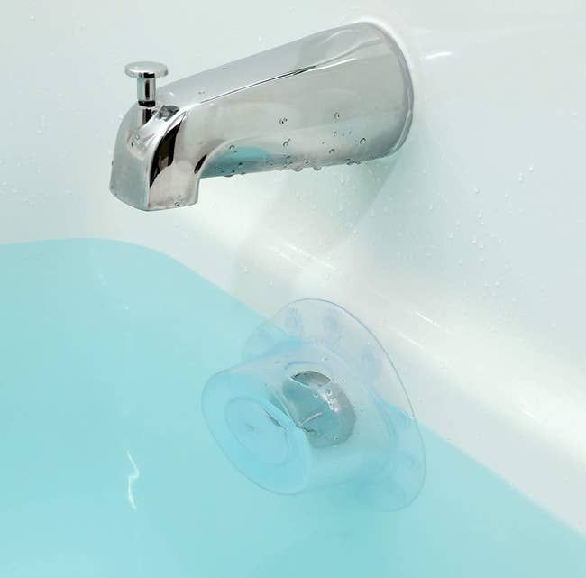 The clear drain cover securely placed over the drain of a full bathtub.