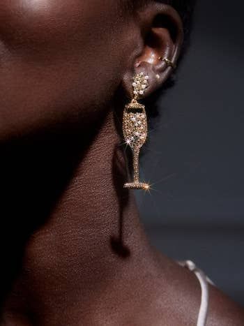 A close-up of a person wearing sparkling earrings shaped like a champagne flute, highlighting luxurious accessories perfect for special occasions