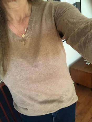 An individual dressed in a V-neck sweater, accessorized with a pendant necklace