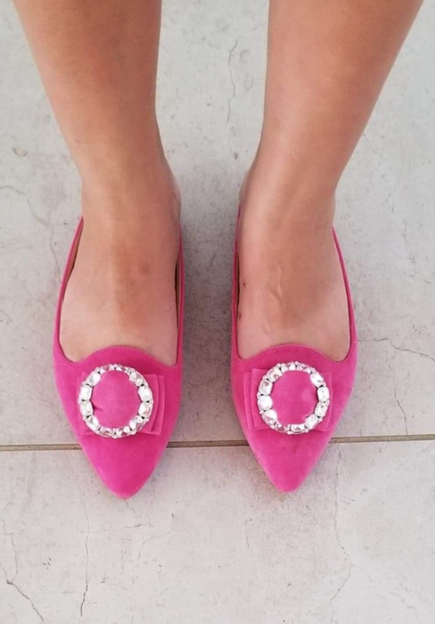 reviewer wearing the pointed-toe slip-on flats in pink suede-like material with a circular embellishment on top