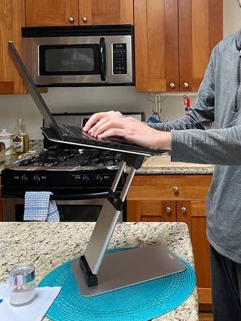 a person using a standing laptop desk on a kitchen counter for an ergonomic work setup
