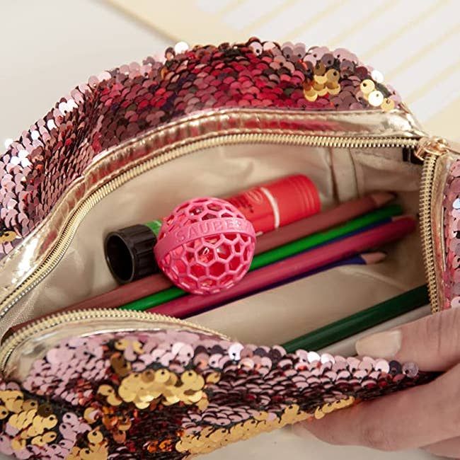 A small pink ball with holes, resting at the bottom of a purse.
