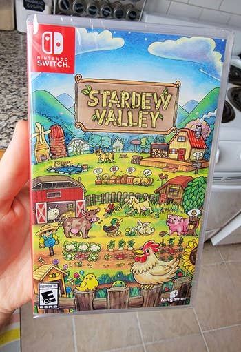 a hand holding a copy of Stardew Valley for the Switch