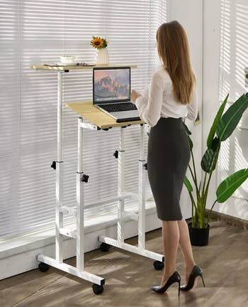 a model at a standing desk with a laptop placed on the bottom tier