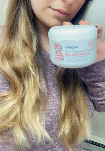 A reviewer with wavy hair holding the jar of the miraculous product