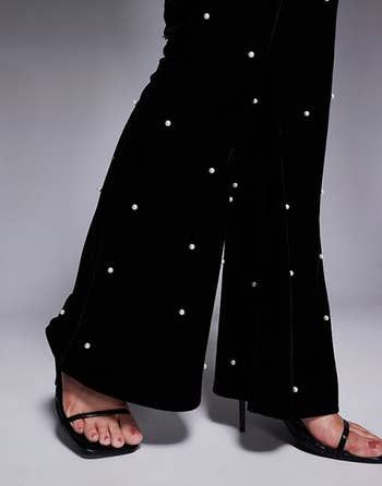 Pearl-adorned velvet pants paired with open-toe heels make a bold fashion statement, perfect for a chic shopping feature.