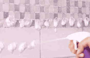 A model spraying foam onto a dirty shower and wiping it clean.