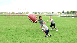 A group of three children enjoy playing with an enormous inflatable football in an open grassy field.