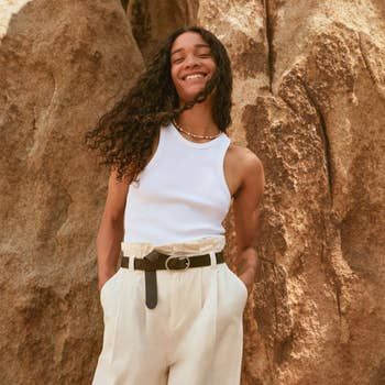 A model rocking a white tank top paired with belted cream paperbag pants for a relaxed, stylish look.
