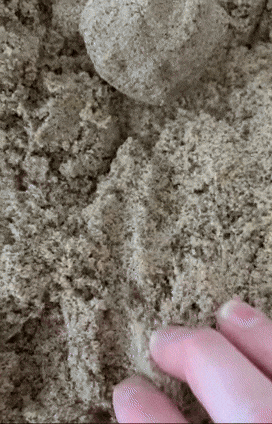 A close-up of a hand gently shaping and smoothing a ball of kinetic sand, feeling its unique texture as it molds into different forms.