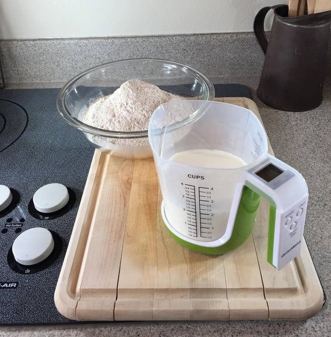A transparent plastic measuring cup placed on a white and green digital scale with a handle.