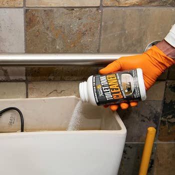 The toilet tank cleaning product being poured into the tank.