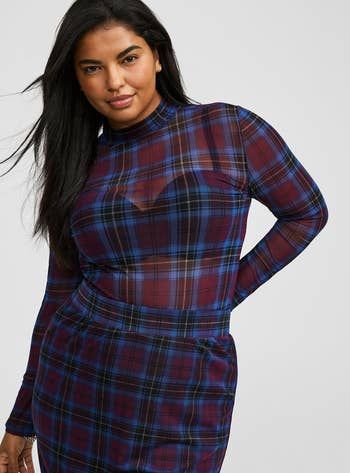 A model confidently poses in a chic plaid dress with a high collar, epitomizing modern elegance.