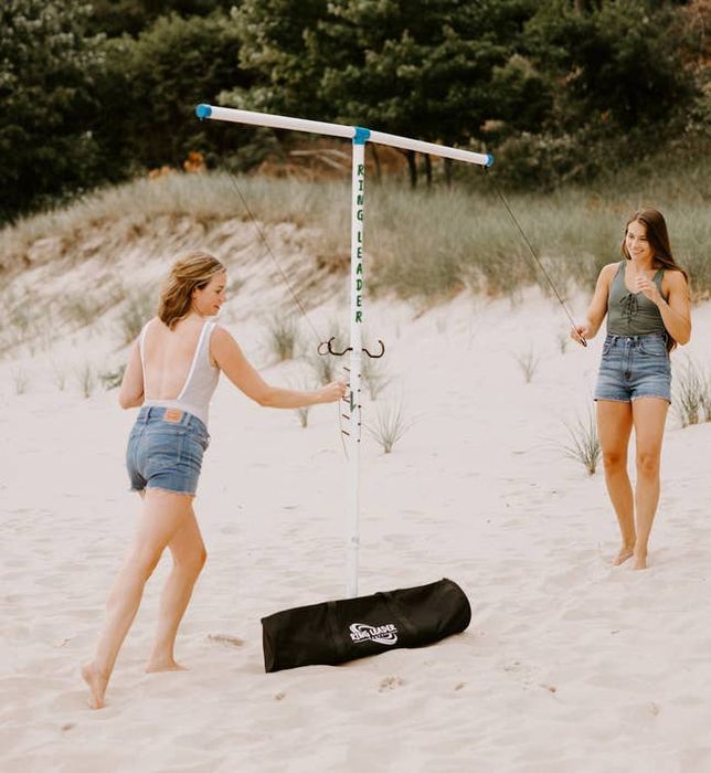 Two models enjoy playing with a portable swingball set on a sandy beach.