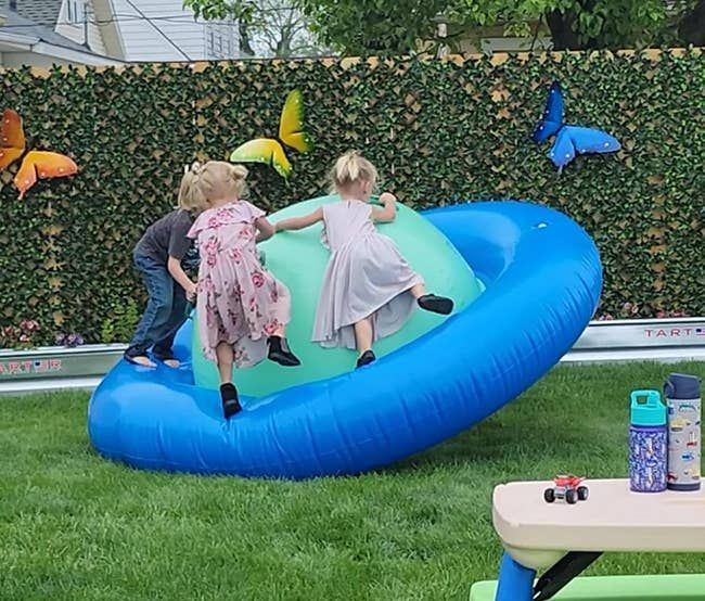 Three children playing on a large inflatable Saturn toy in a backyard