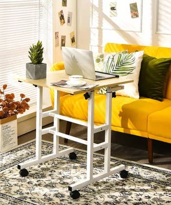 A height-adjustable standing desk with wheels positioned next to a couch