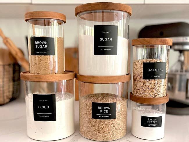 Black minimalist pantry labels placed on jars filled with a variety of dry goods.