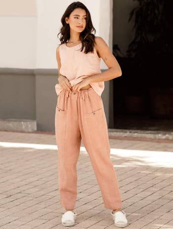 A model is showcasing coral-colored pants paired with a peach tank top and white sneakers.