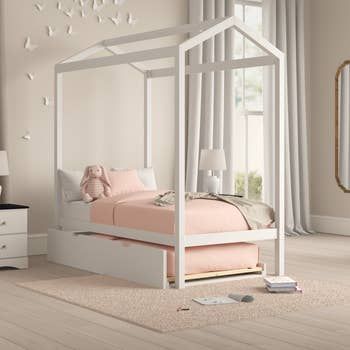 A white canopy bed with a trundle, beautifully placed in a kid's bedroom.