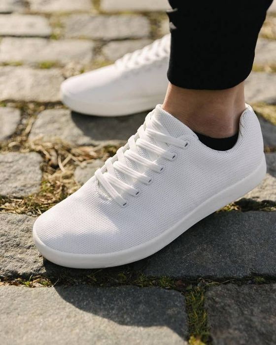 All white sneakers worn by a model with black socks.