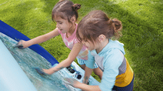 Two young children engaged in painting on an inflatable canvas outdoors, before the hose cleans it all up.