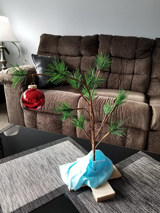 A reviewer photo of the Charlie Brown Christmas tree, adorned with a single red ornament, with Linus' blue blanket elegantly draped around the base