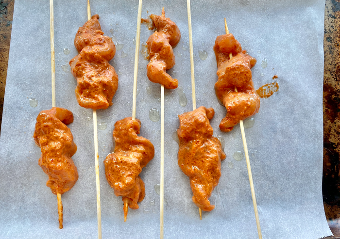Raw chicken marinated in Thai curry, then skewered on a baking sheet.