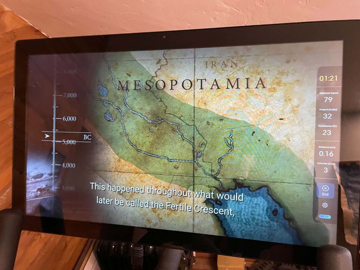Image of a Peloton display streaming a show (featuring a map of Mesopotamia) with cycling statistics displayed in a vertical bar on the right side of the screen.