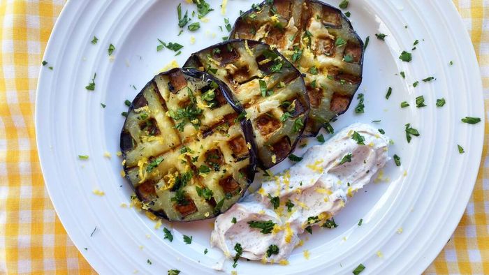 A plate showcasing multiple slices of waffled eggplant accompanied by a dollop of creamy white dip, garnished with fresh herbs