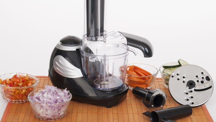 A food processor placed next to small bowls filled with chopped vegetables