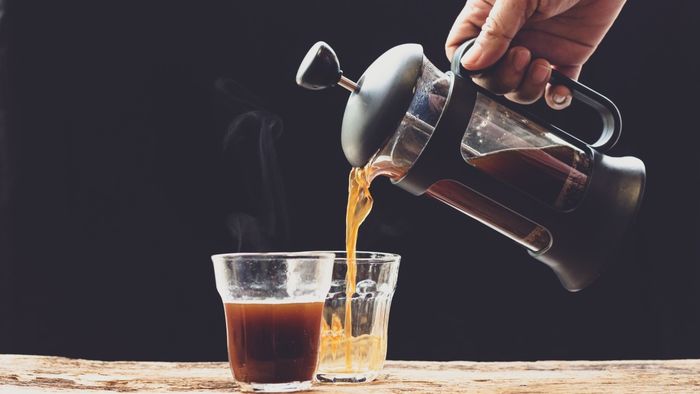 A hand gently pouring freshly brewed French press coffee into two transparent cups.