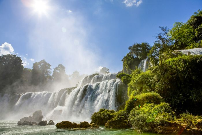A majestic waterfall straddling the border between Vietnam and China, with a massive flow of water cascading over its edge.