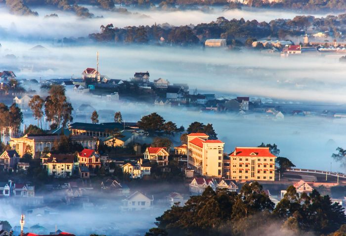 An aerial perspective over the hill station of Dalat in Vietnam, where the town is enveloped in mist due to its high elevation, leaving only a few buildings visible.