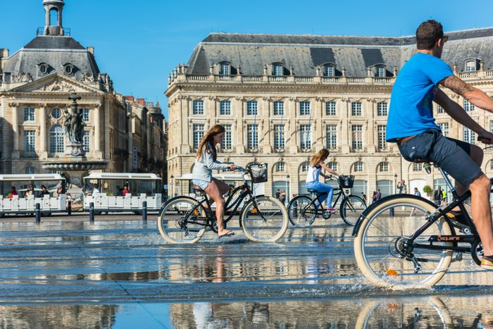 Cyclists enjoy the mirror fountain in front of Place de la Bourse in Bordeaux, France