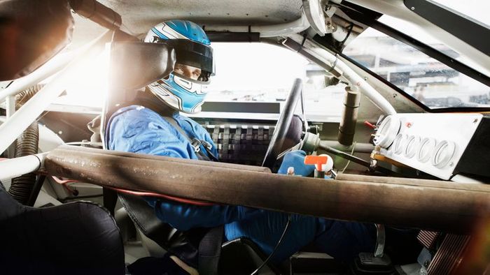A professional race car driver seated in the cockpit of a high-speed vehicle.
