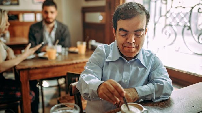 A businessman with dwarfism enjoying a cup of coffee at a local café.