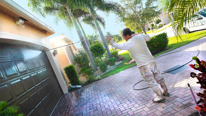 A person cleaning a weathered brown garage door with a pressure washer.