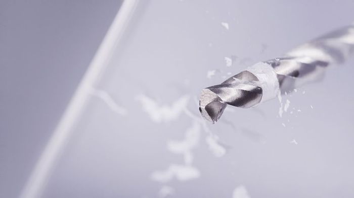 A drill bit making its way through a sheet of glass.