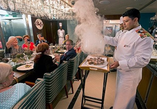 a chef presenting a freshly prepared steak at the chef’s table aboard the Dinogo Spirit