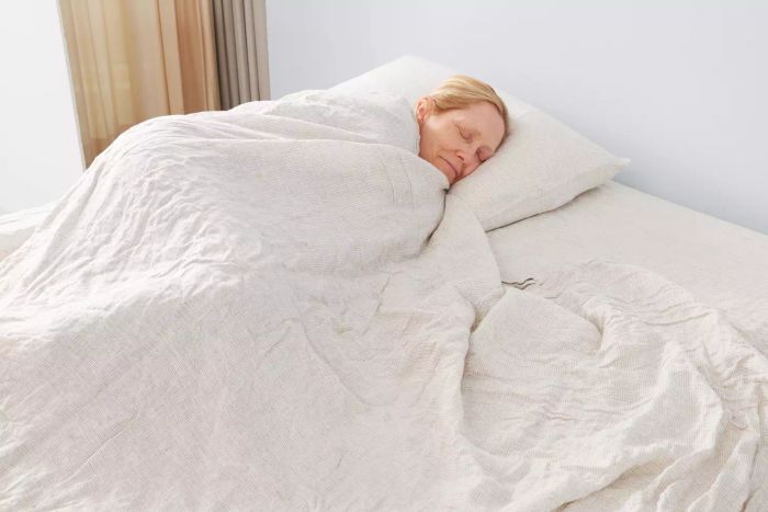 A person resting comfortably on the Crate & Barrel Garden Green Grid Natural Hemp Fiber Queen Bed Sheet Set.