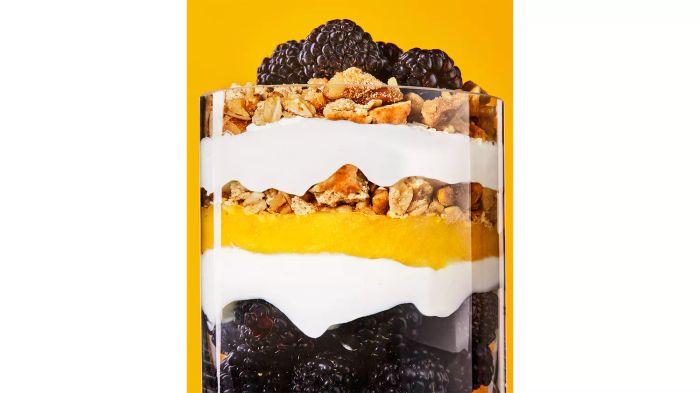 A glass cup filled with lemon curd and berries, showcasing the distinct layers inside.